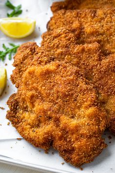 some fried food on a white plate with lemons and parsley next to it