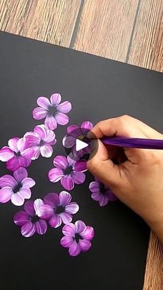 a person is drawing flowers on a piece of black paper with purple crayons