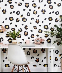 a white table topped with a plant next to a wall covered in black and yellow flowers