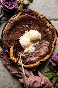 a chocolate pie with ice cream on top and purple flowers in the backgroud