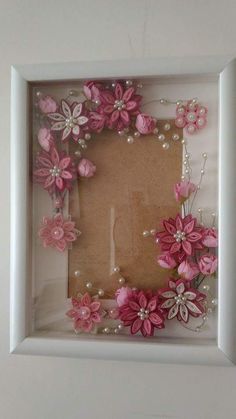 a white frame with pink flowers and pearls on the bottom is hanging in front of a wall