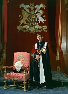 a man dressed in an elaborately decorated uniform sitting next to a chair with a stuffed animal on it