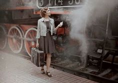 a woman standing next to a train with steam coming out of it