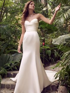 a woman in a white wedding dress standing on some steps with her hand out to the side