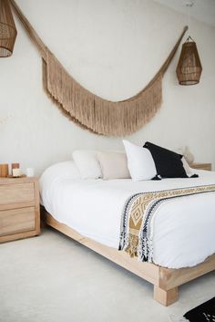 a bed with white sheets and pillows in a bedroom next to two hanging baskets on the wall