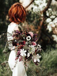 a woman with red hair holding a bouquet of flowers and greenery in her hands