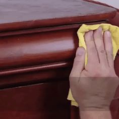 a person with a yellow cloth on their hand wiping the top of a wooden table