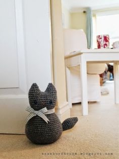 a crocheted cat sitting on the floor in front of a white door and table