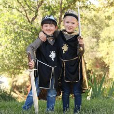 two young boys dressed up in medieval clothing holding swords and shield, posing for the camera