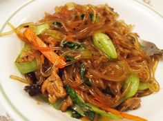 a white plate topped with noodles and veggies next to a fork on top of a table