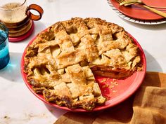 a pie with one slice cut out on a plate next to two glasses and utensils