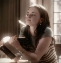 a woman sitting at a table with an open book in her hand and looking up