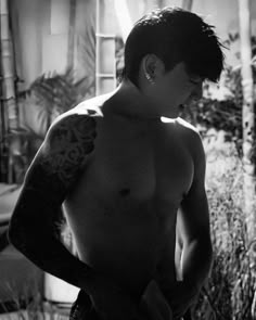 black and white photograph of a man with tattoos on his arm standing in front of a potted plant