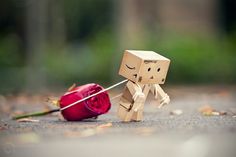 a small cardboard man pulling a red rose on the ground with it's end