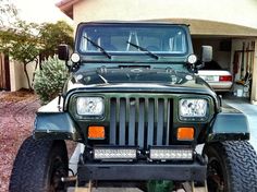 a green jeep is parked in front of a house with its lights on and the hood up