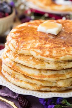 a stack of pancakes with butter on top and berries in the background, ready to be eaten