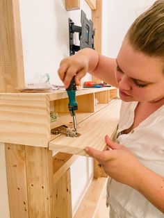 a woman is working on some wood with a drill and screwdriver in her hand