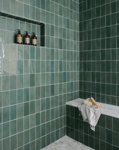 a green tiled bathroom with white towels and soap bottles on the shelf next to the bathtub