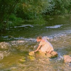 a woman in white dress sitting on rock next to river