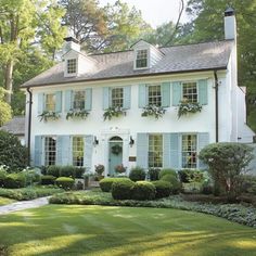 a large white house with blue shutters and green grass in the front yard area