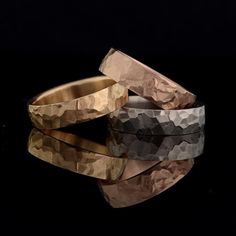 two gold wedding bands sitting next to each other on top of a black surface with the words mccaugldsmiths