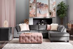 a living room with grey couches and pink accents on the walls in front of a fireplace