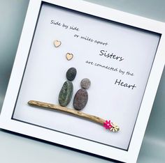 two rocks sitting on top of a wooden stick in front of a white framed frame