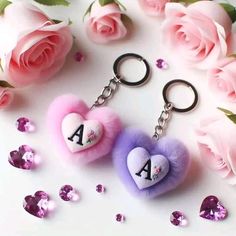 two heart shaped key chains sitting next to pink roses and purple hearts with the letter a on them