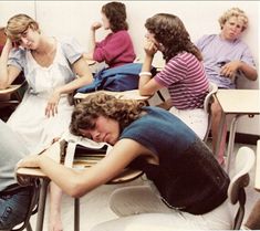 a group of people sitting at desks in a classroom with one person asleep on the floor