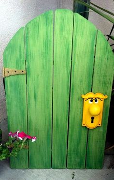 a green door with a yellow face on it and a flower in the foreground