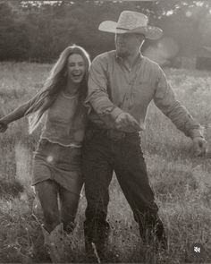 black and white photograph of man and woman walking through field with cowboy hat on head