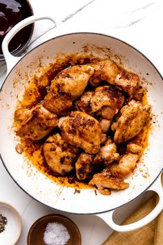 chicken in a pan with spices and seasoning on the side next to two mugs