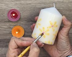 someone is painting a candle with yellow flowers on it and two candles are next to them