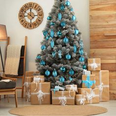 a christmas tree with presents in front of it and a clock on the wall behind it