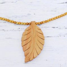 a wooden necklace with a large leaf on it's beaded cord, hanging from a white wood background