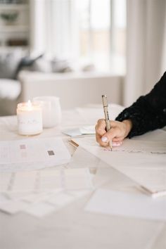 a person writing on paper with a pen in their hand and a candle next to it