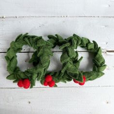 two green wreaths with red berries hanging from them on a white wooden background,