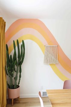 a potted cactus sitting next to a wall with a rainbow painted on it