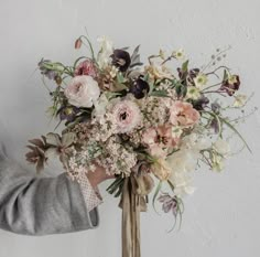 a person holding a bouquet of flowers in their hand and wearing a gray cardigan