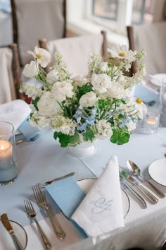 a vase filled with white flowers sitting on top of a table next to silverware