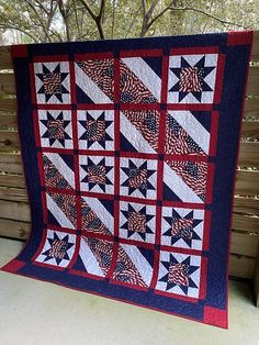 a red, white and blue quilt hanging on a wooden fence next to a tree