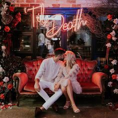 a man and woman sitting on a couch in front of a neon sign