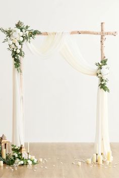 a white wedding arch decorated with flowers and greenery on the floor next to candles