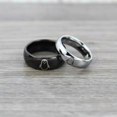 two wedding rings sitting on top of a wooden table next to each other, one with a penguin in the middle