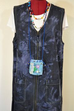 a black vest with a blue tie dye pocket and beaded necklace hanging from it