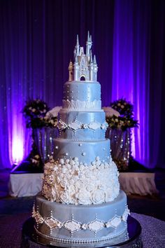 a blue wedding cake sitting on top of a table next to purple drapes and flowers