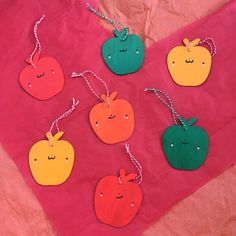 four apples and two oranges are hanging from twine strings on a pink background