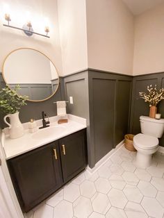 a white toilet sitting next to a bathroom sink under a round mirror in a bathroom