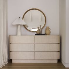 a dresser with a mirror, lamp and vases on it in a white room