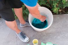 a person standing over a bucket filled with blue colored liquid next to other items on the ground